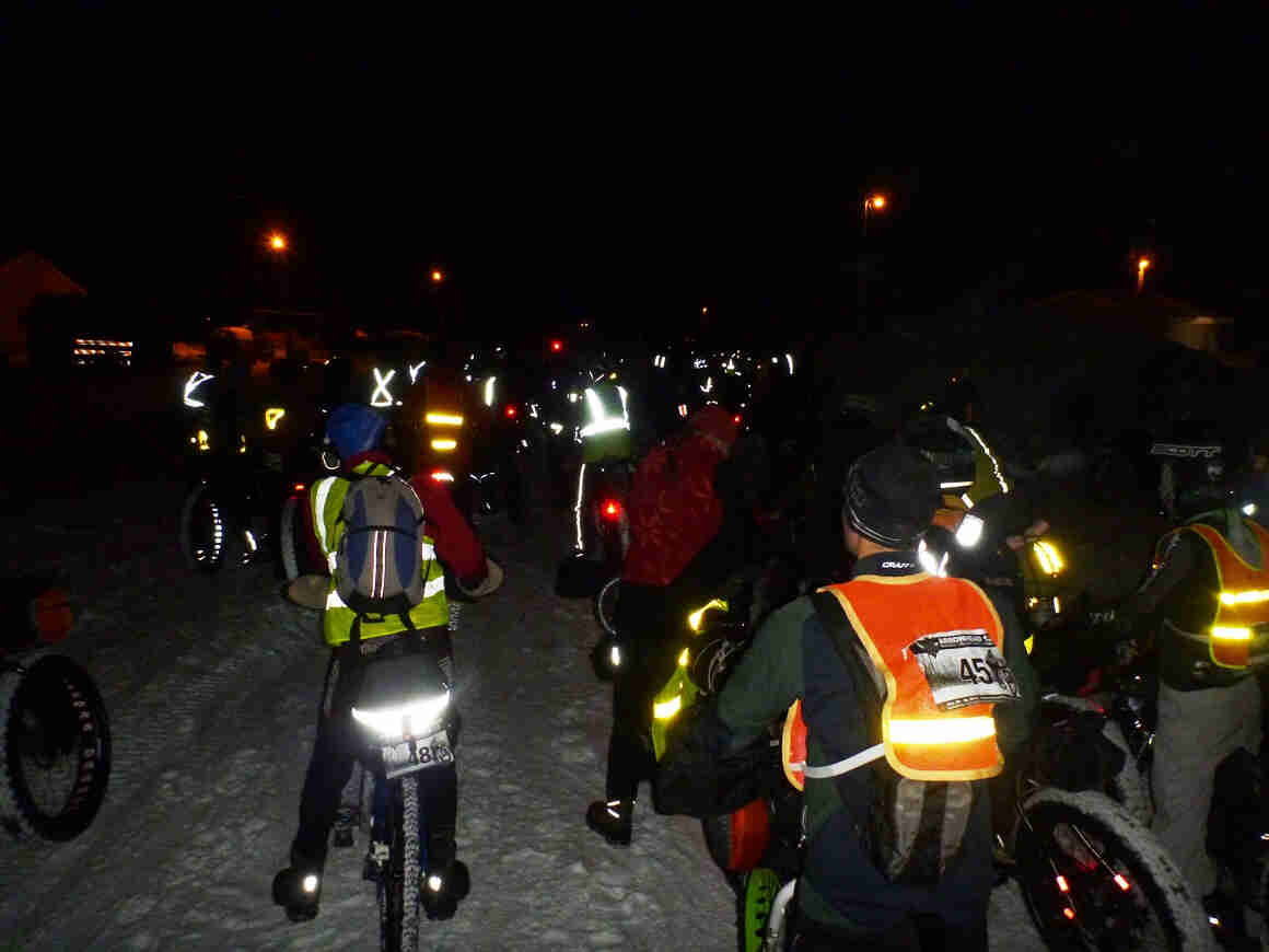 Rear view of a group of winter cyclists, standing over their bikes on snow, at nighttime