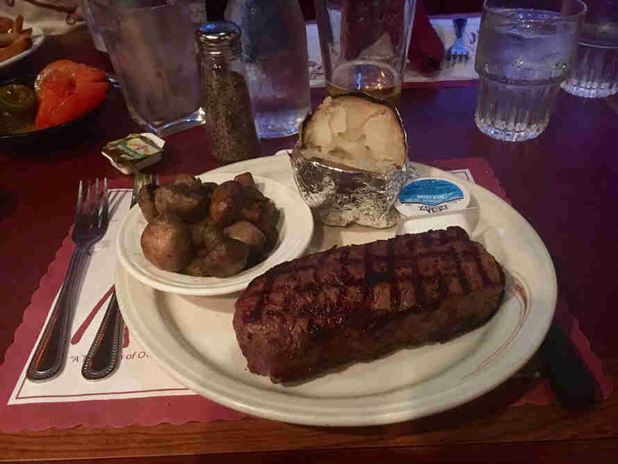 A steak, mushrooms and a baked potato, on a plate