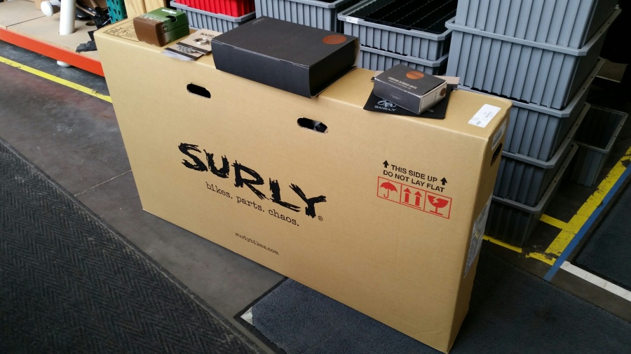 A Surly bike box on a sidewalk, with plastic totes in the background