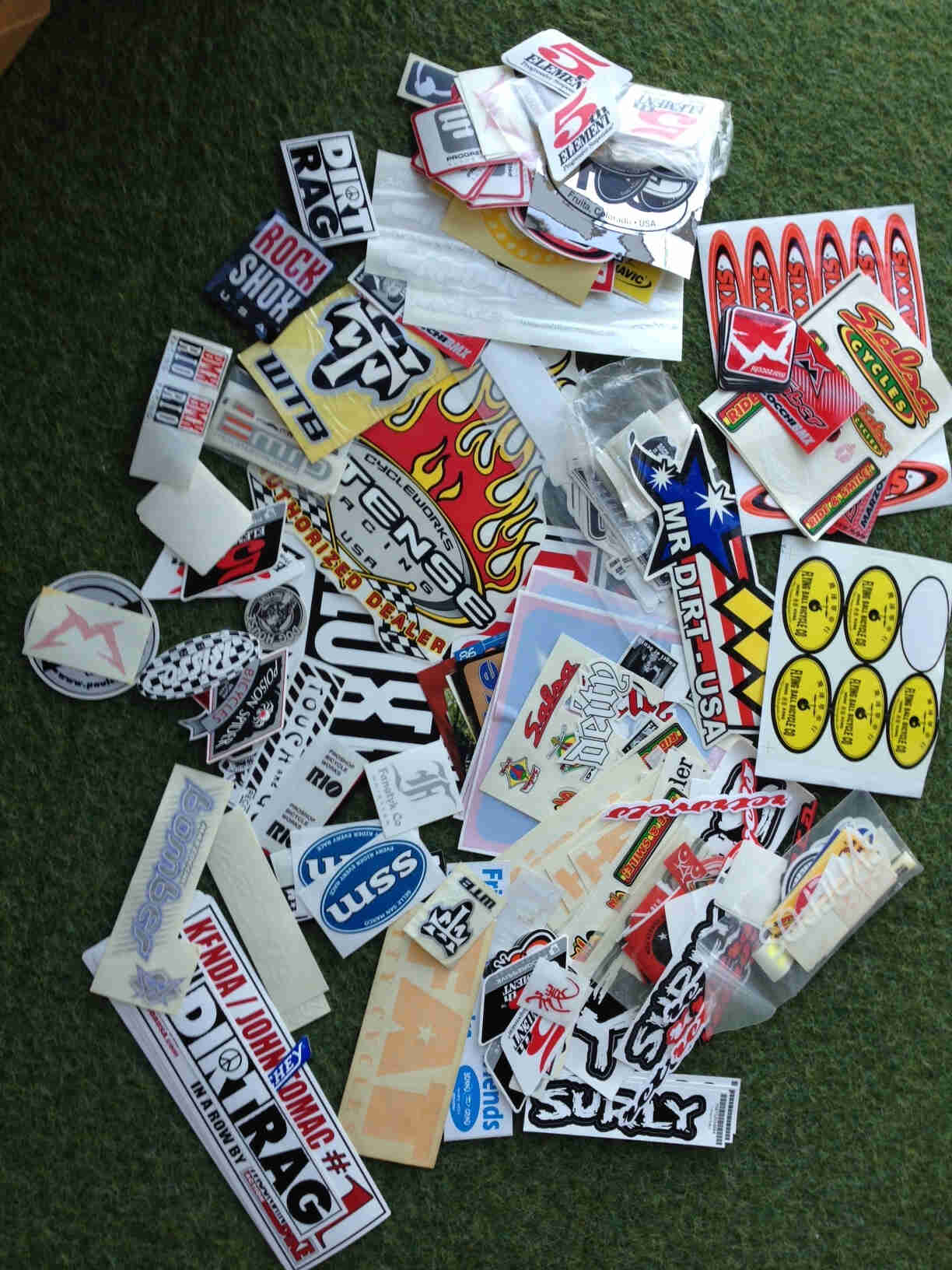 A collection of stickers, scattered on laying flat on each other, on top of a green surface
