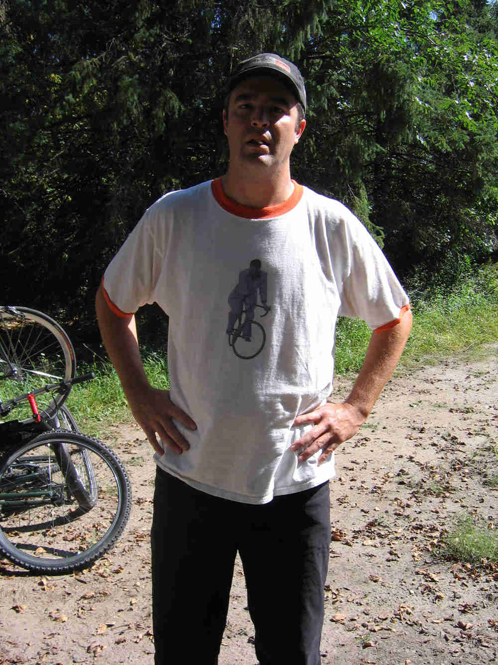 Front view of a person wearing a white t-shirt with a bicyclist on it, with trees in the background