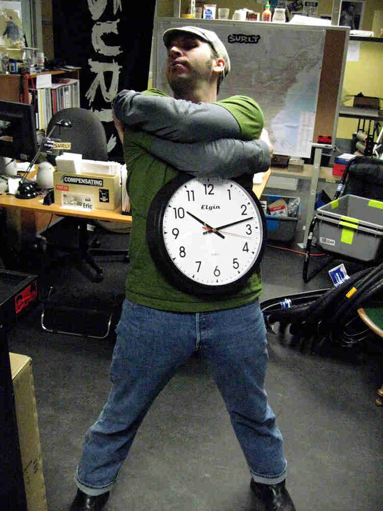 Front view of a person with their arms crossed, with a clock on their torso, in an office