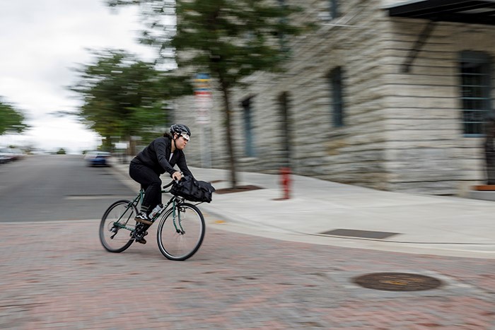 Front, angled, right side view of a cyclist on a green Surly Pack Rat bike, making a swift left turn on a city street