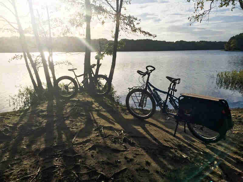 Left side view of a Surly Big Dummy bike, parked on dirt bank of a lake, next to another bike