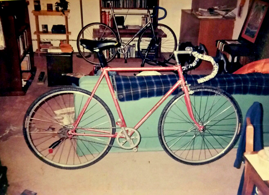 Right side view of a red road bike leaning on the back of a couch in a room, with another bike in the background