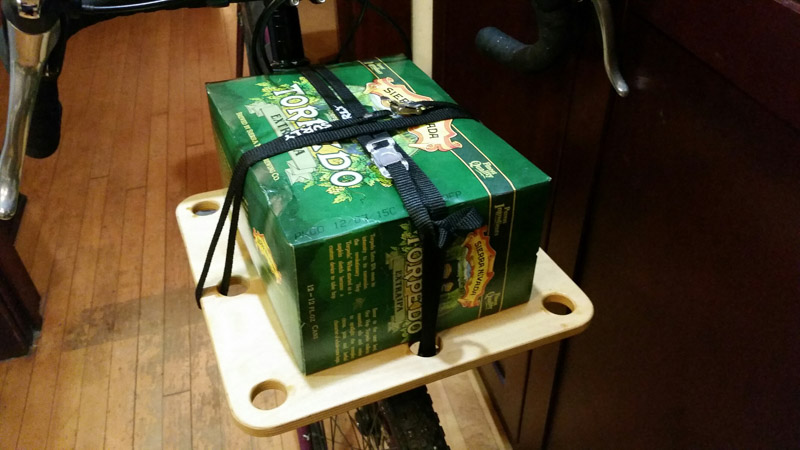 A Surly Junk strap - black - holding down a 12 pack of beer on top of a bike rack