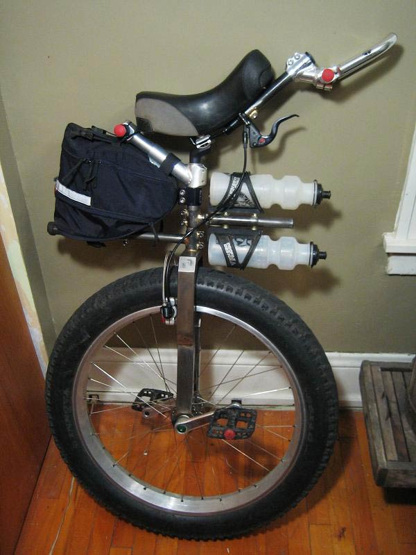 Right side view of a fat wheeled unicycle, parked in a room with wood floors, next to a wall