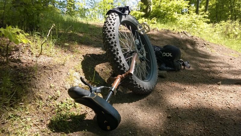 A unicycle with a fat bike wheel, laying down on a dirt trail in the woods