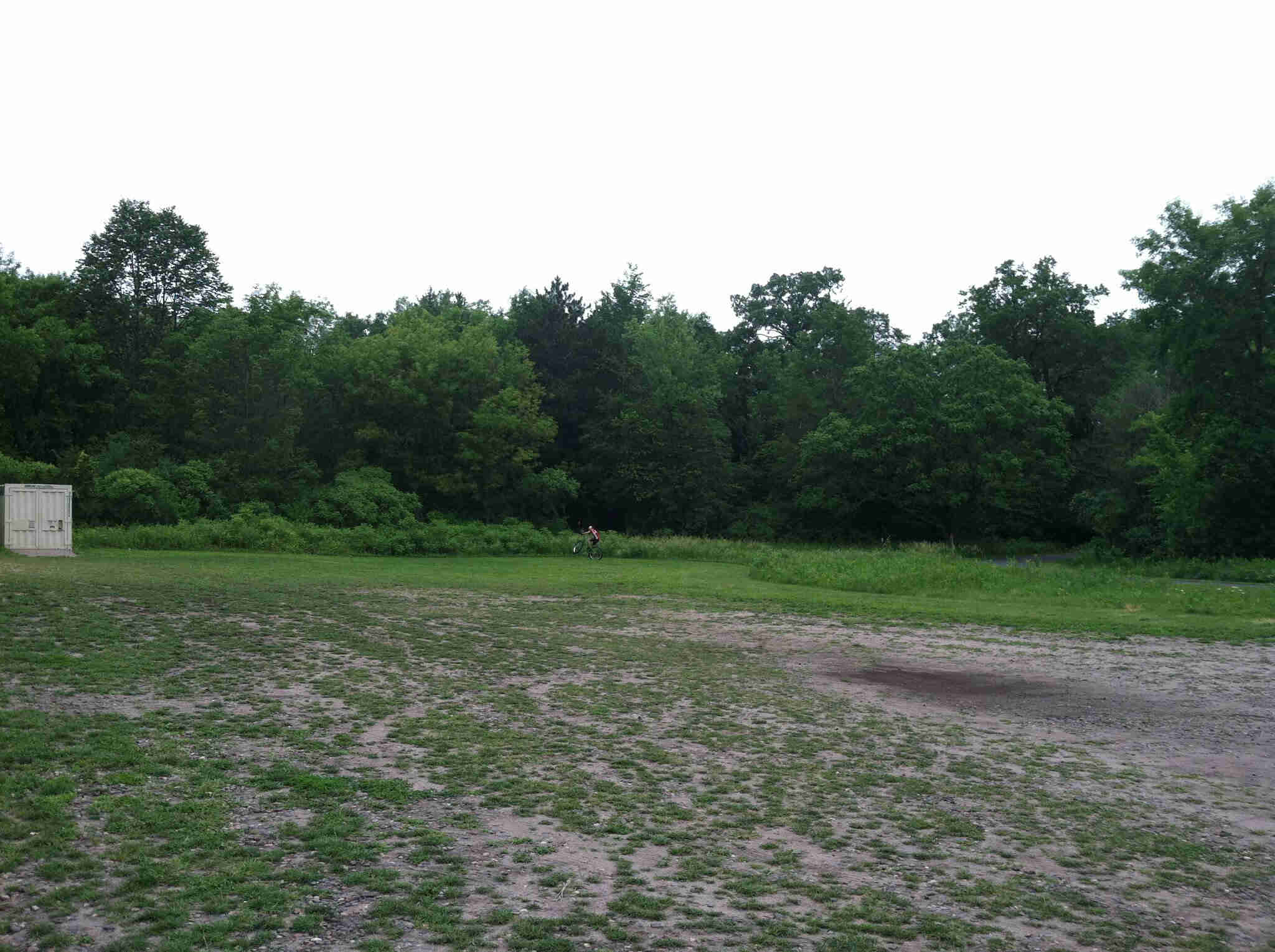 A dirt and grass field with a cyclist in the distance, riding a Surly Krampus bike across a tree line