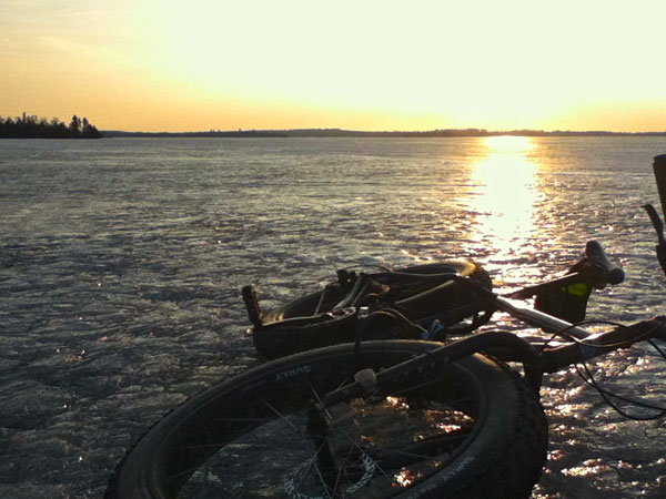 Front, right side view of a Surly Moonlander fat bike, laying on a frozen lake at sunset