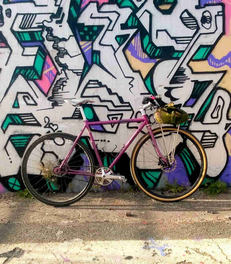 Right side view of a raspberry color Surly bike, leaning against a wall with colorful graffiti