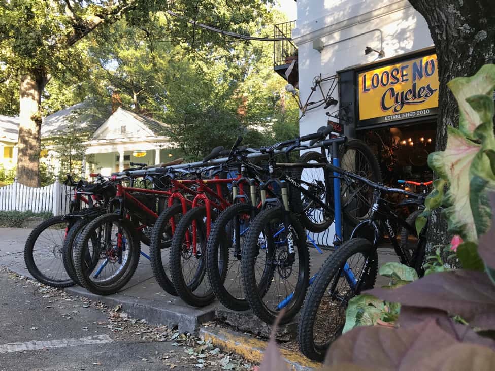 Bikes lined up side by side in a rack, on a sidewalk, with the Loose Nuts bike shop in the background