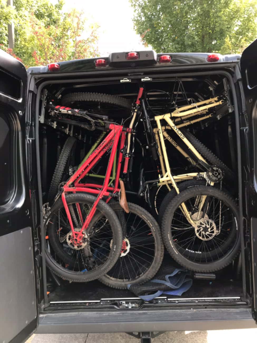 Rear view of a van with the rear doors open, showing Surly bikes packed in, seat to seat, from top to bottom