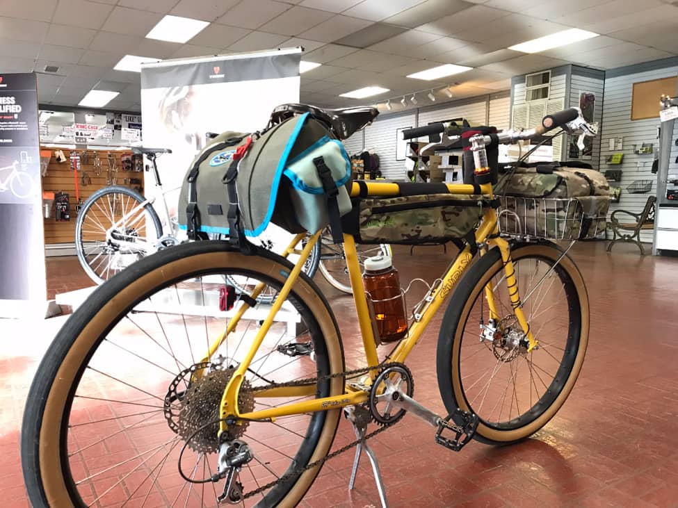 Right side angled view of a yellow Surly bike with gear, on the red brick floor of a bike shop showroom