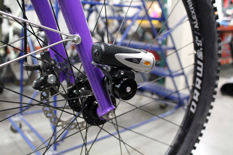 Right side view of the bottom half a purple bike fork with a light mounted and a wheel