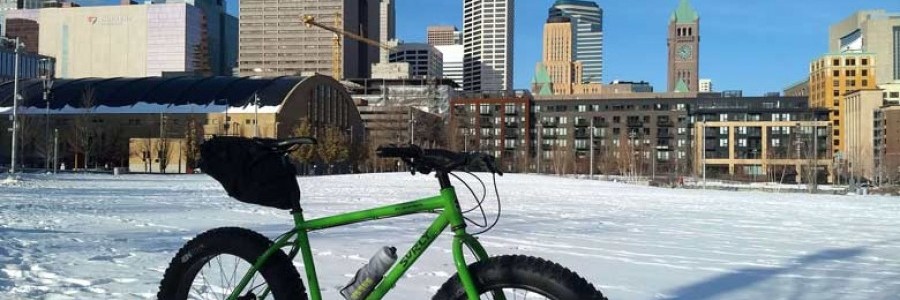 Surly Ice Cream Truck bike, green, with seat pack and water bottle, in snowy field with buildings in background