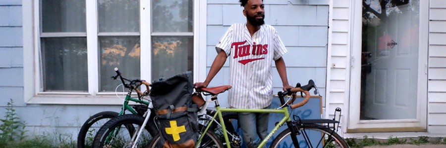Wesley stands in front of house wearing Twins jersey with lime color Surly bike in front of him and 2 bikes behind him