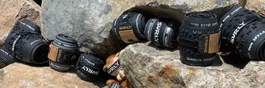 Black Surly bike tires in rolls between boulders and with a stuffed animal doll with a plastic wearing a Surly headband
