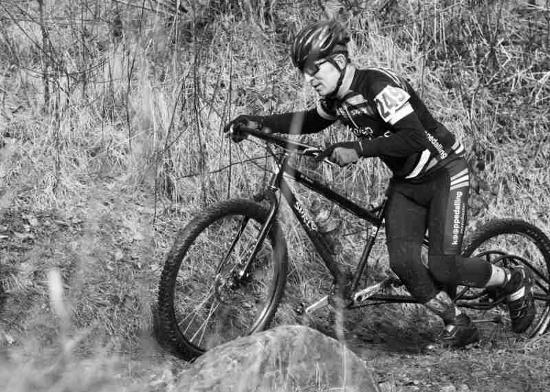 Left side view of a Surly Big Dummy bike, with a race cyclist pushing it up a dirt trail - black & white image