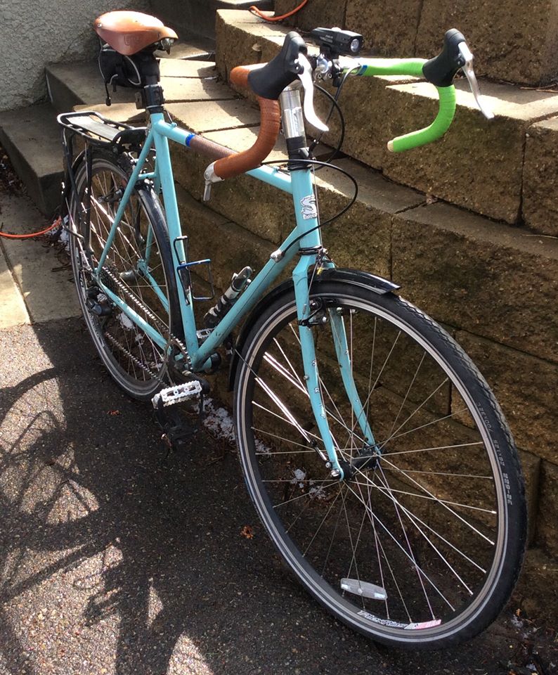 Front, right side view of a light blue Surly bike with fenders, parked against a wall constructed of landscape block