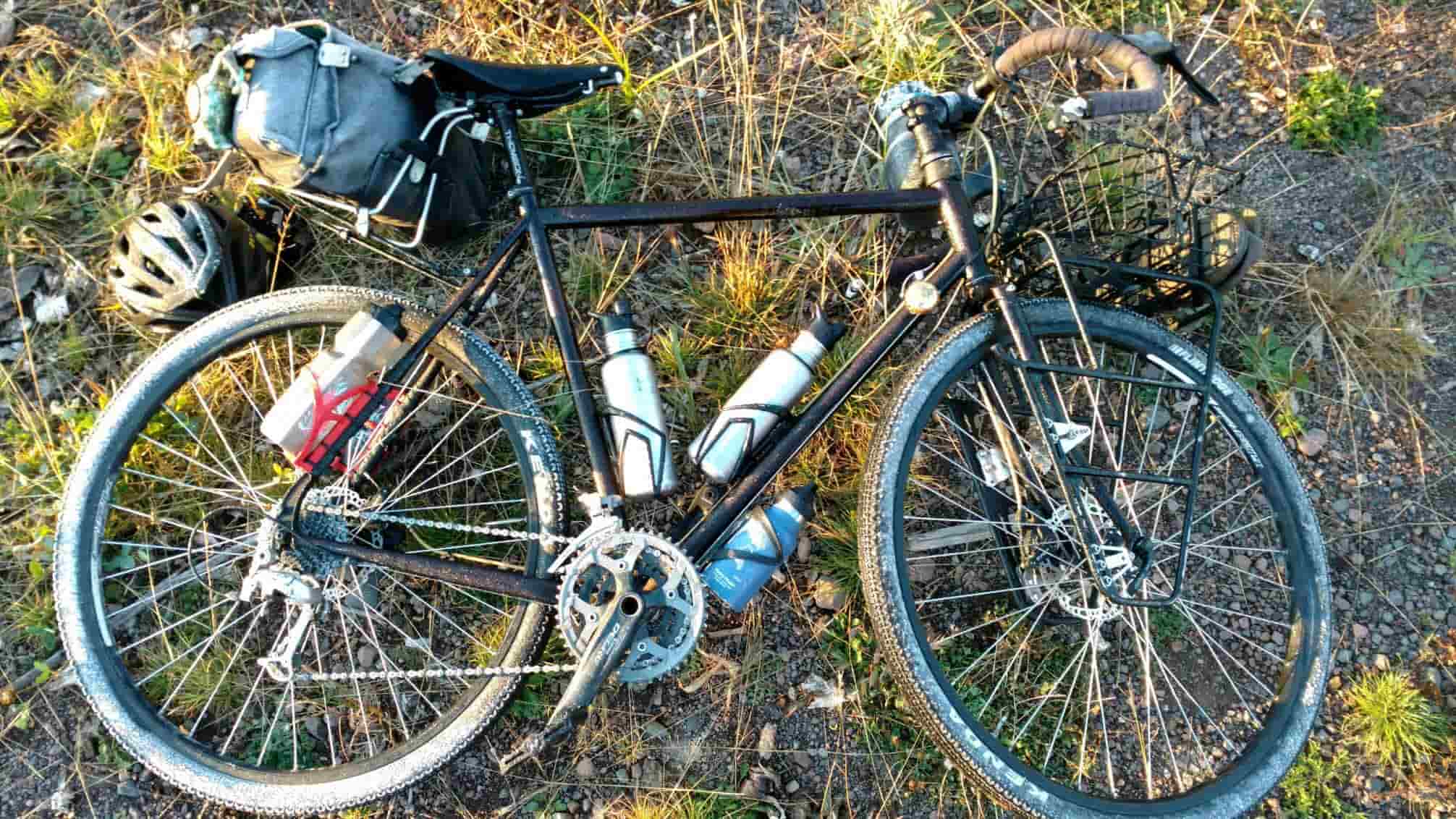 Downward left side view of a bike loaded with gear, laying on it's left side in gravel and weeds
