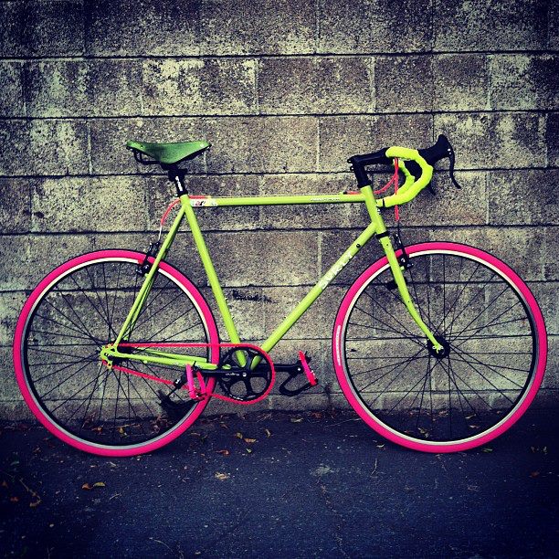 Right profile of a lime green Surly Cross Check bike with pink tires, leaning against a cinder block wall