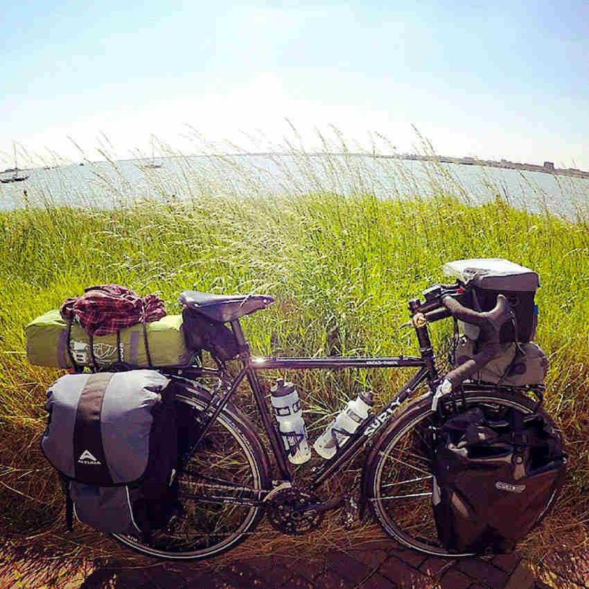 Right side view of a black Surly Cross Check bike with gear packs, parked next to tall grass, with a lake in background