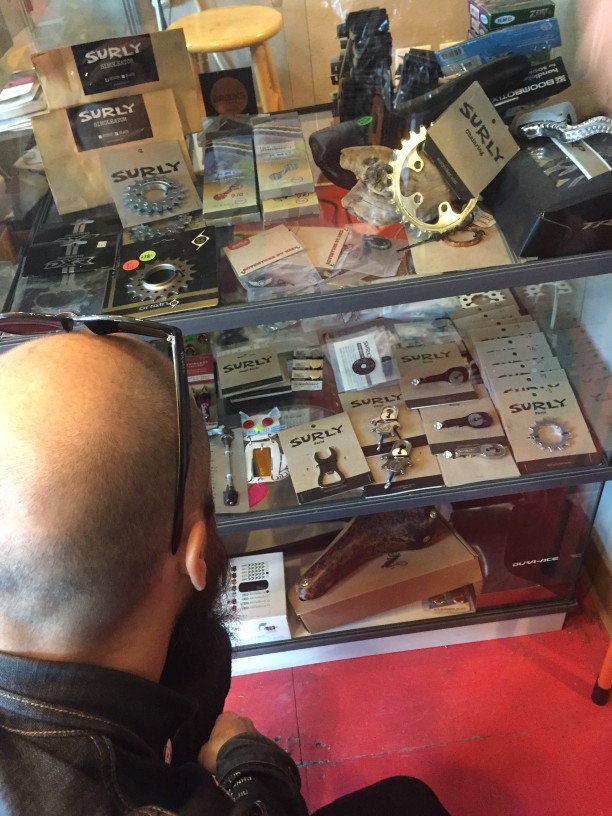 Downward, rear view of a person looking at a shelf unit full of Surly bike parts