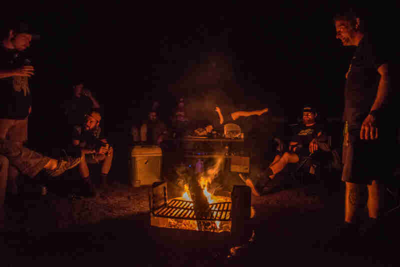 A group of people standing and sitting around a campfire at night