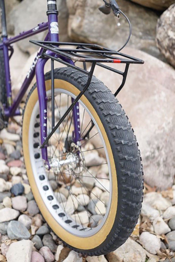 Front angle view of left side of purple Surly Pugsley fat bike with a fork carry rack, parked on rocks