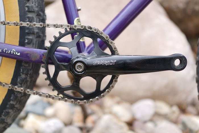 Close up of a black Surly crankset with a portion of the chain and rear tire on a purple Pugsley fat bike