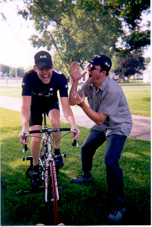 A person yelling in the ear of a cyclist riding a bike on grass