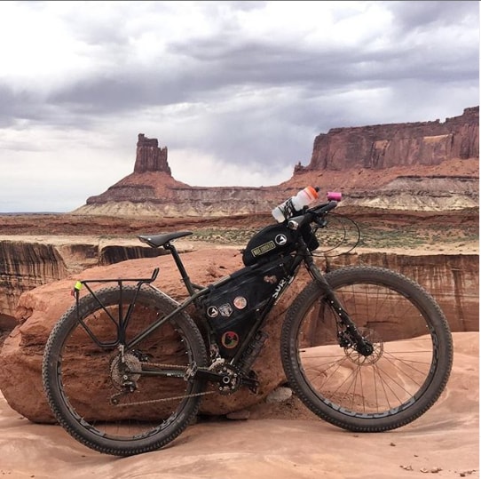 Right side view of a black Surly ECR bike loaded with gear leaning  on a large rock on the edge of a desert canyon 