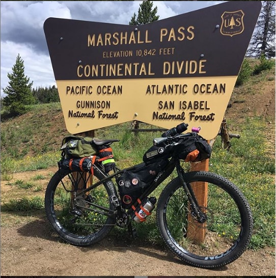 Right side view of a black Surly ECR bike loaded with gear leans on a Marshall Pass Continental divide sign