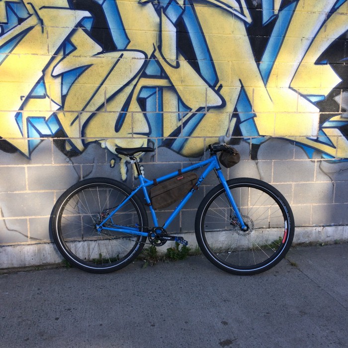 Right side view of a blue Surly bike, parked against a cinder block wall with graffiti