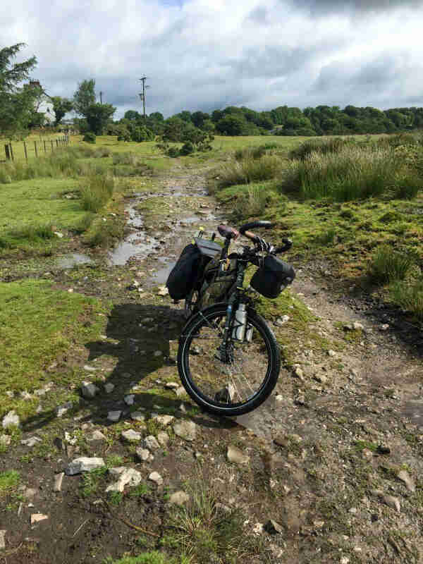 Front view of a Surly Big Dummy bike, parked in a dried up stream bed in a field with trees in the background