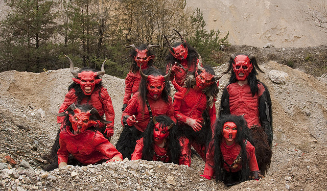 Front view of a group of people, dressed in red Krampus monster costumes, posing together in a small rock pit