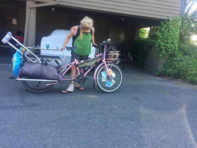 Cyclist with a right broken foot, looks down at a Surly Big dummy bike, pink with a crutch on the rear rack, in front of a garage