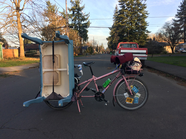 Right side view of a Surly Big Dummy bike, pink, with a blue table on the rear rack, on a street