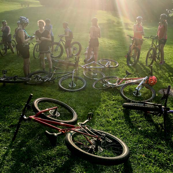 A group of cyclists standing in a grassy field, with their bikes laying around, and a ray of sun shining down on them