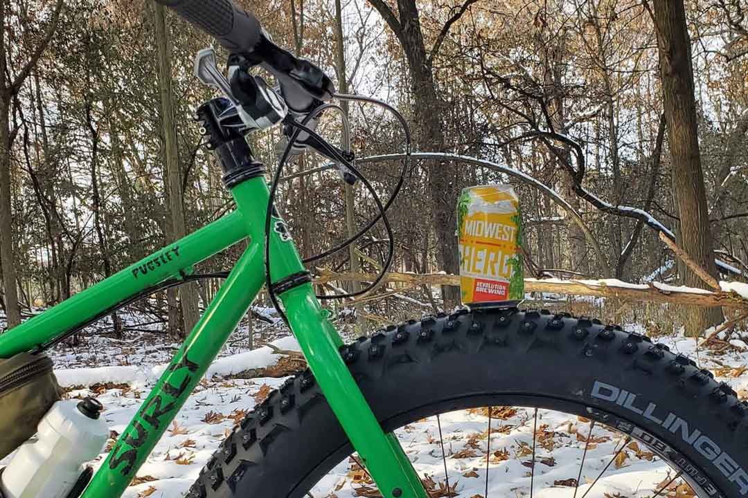 Right side, cropped view of green Surly Pugsley fat bike, with a beer can on the front tire, in the snowy woods