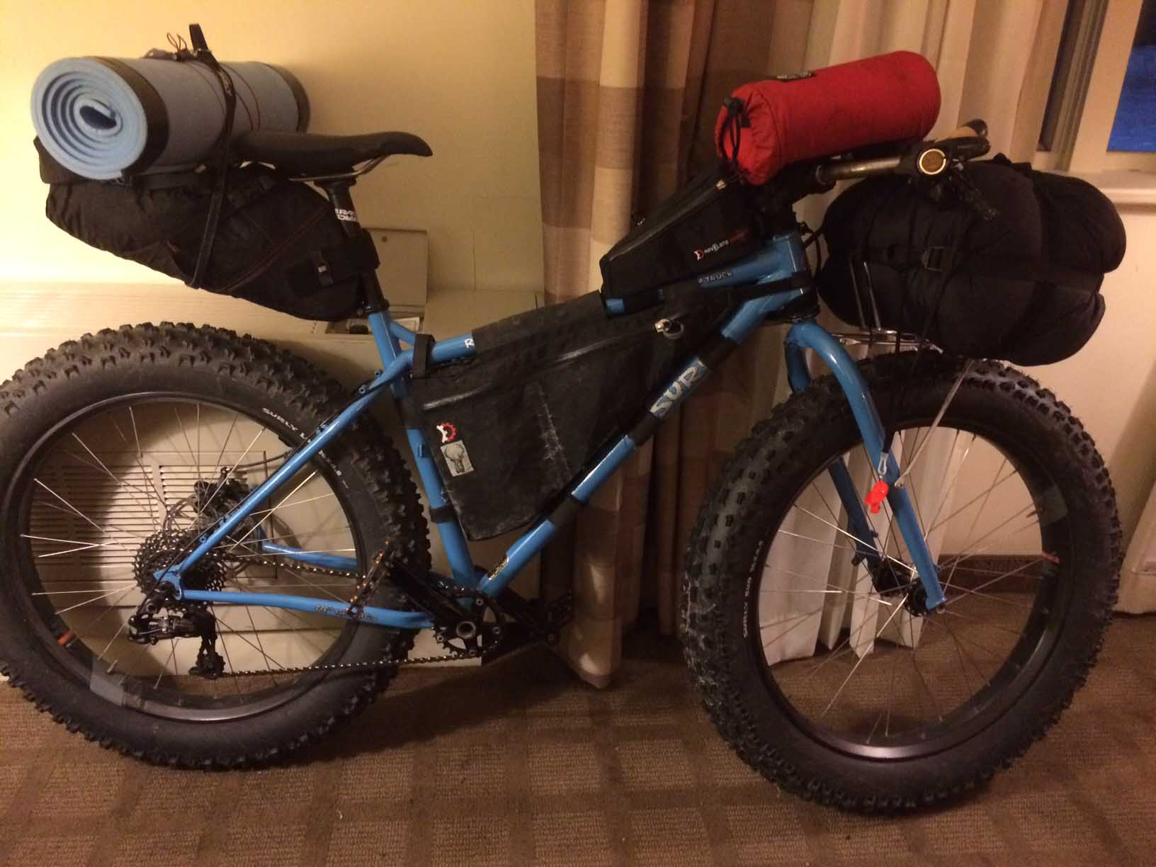 Right side view of a blue Surly Ice Cream Truck fat bike loaded with gear, against a room, against the wall