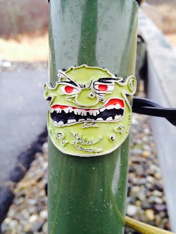 Front, close up view of the head tube of a green Surly Ogre bike, with an ogre emblem attached to it