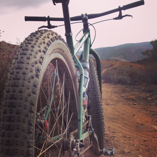Rear view of a green Surly Krampus bike, facing down a dirt trail in the desert hills