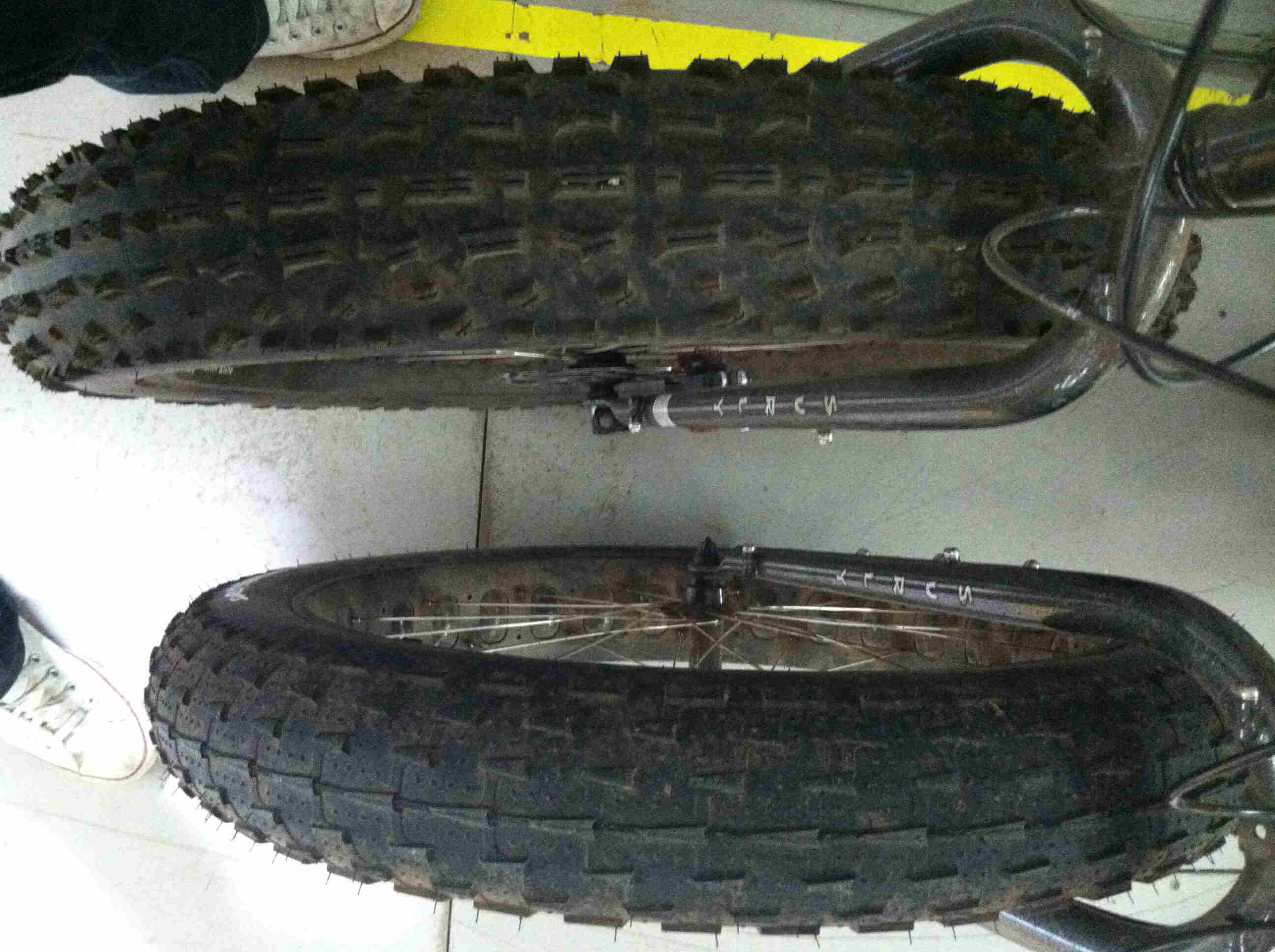 Downward, front end view of the wheels from 2 Surly fat bikes, that are parked side by side on a cement floor