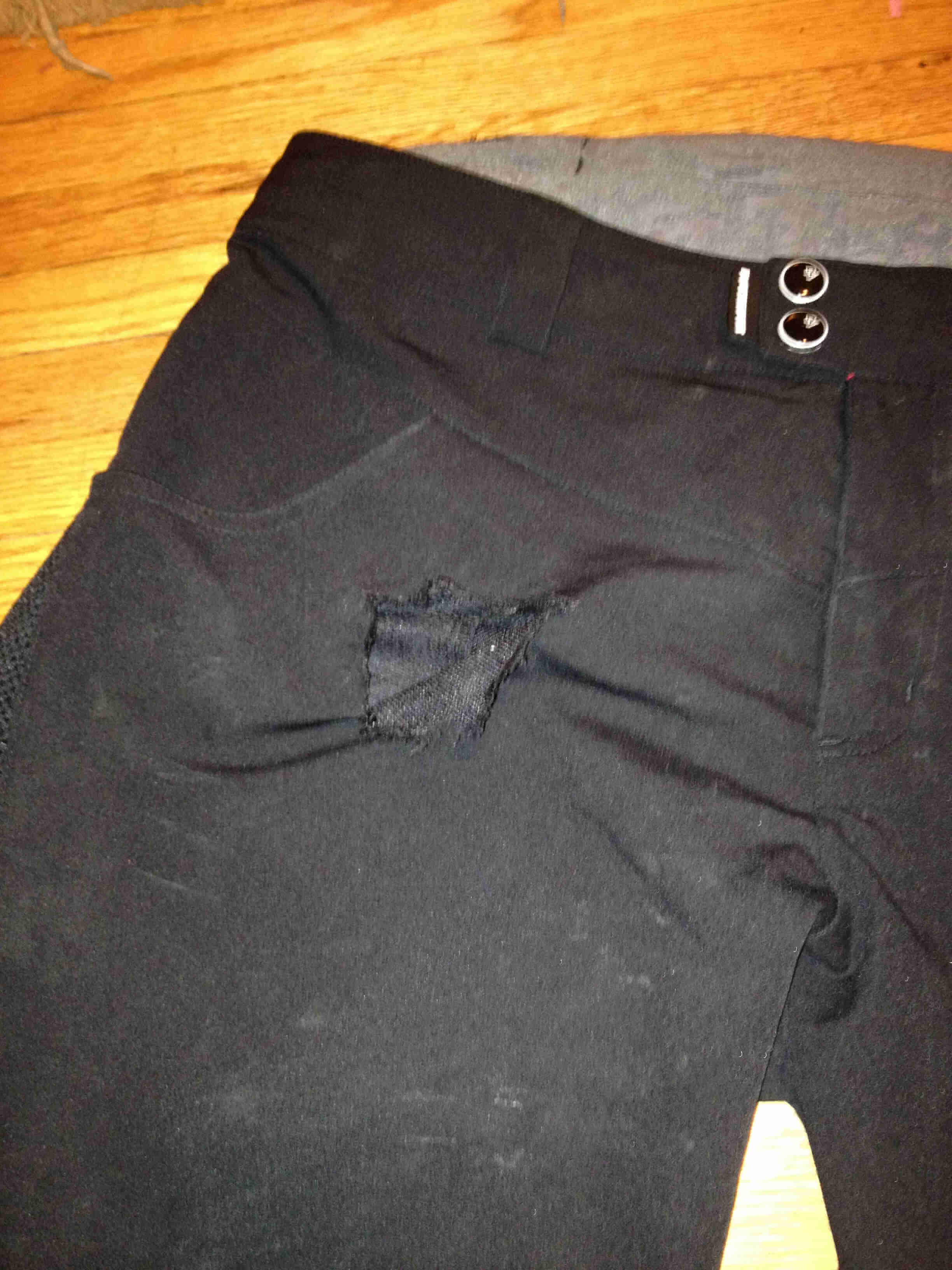 Downward, front, upper right side view of a pair of black shorts, with a tear by the right pocket