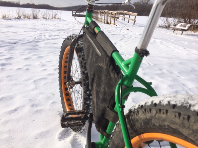 Rear, right side view of a green Surly fat bike, on a snow covered field, facing a wood dock on a frozen lake