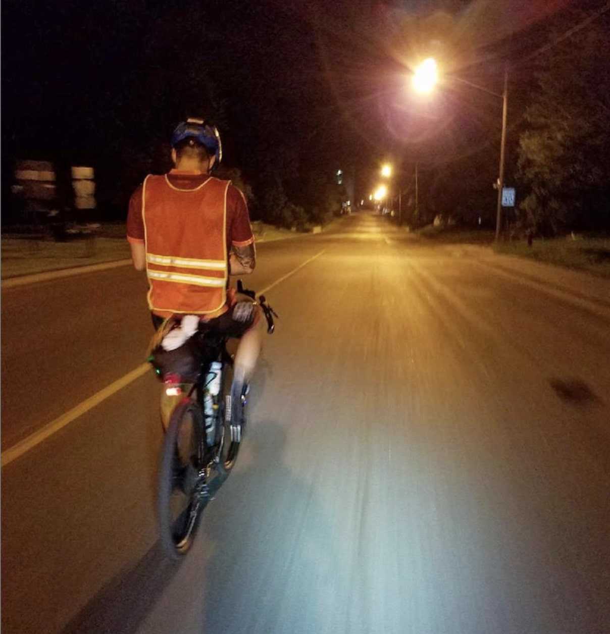 Cyclist wears a reflective vest while riding a bike down a city street at night under the street lights