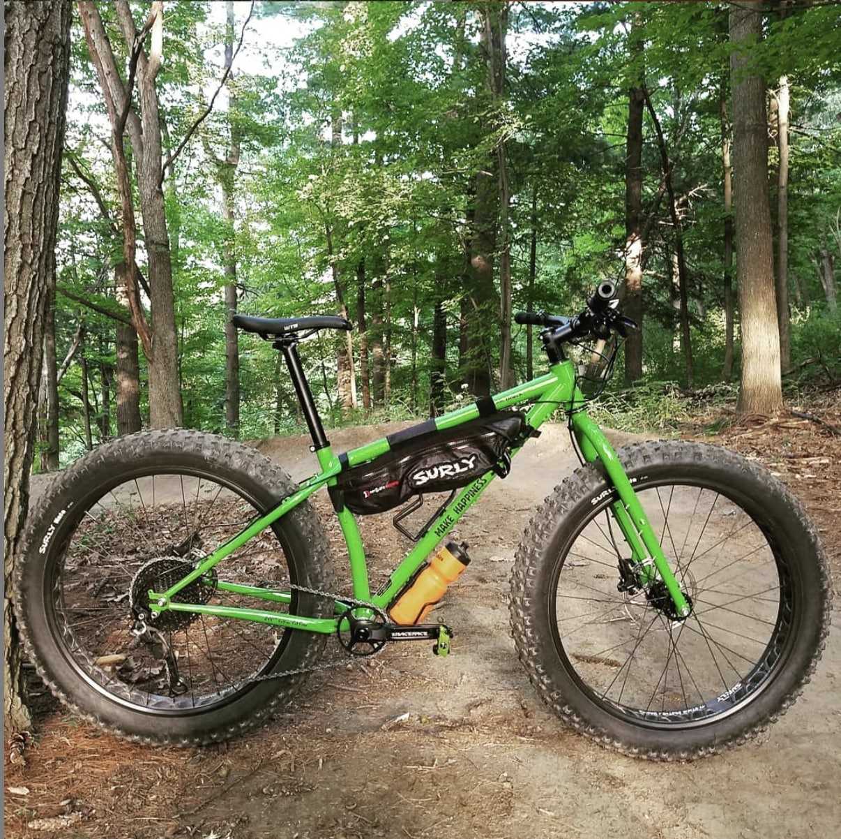 Right side profile view of a green Surly Ice Cream Truck fat bike with gear set on a dirt trail in the pine trees