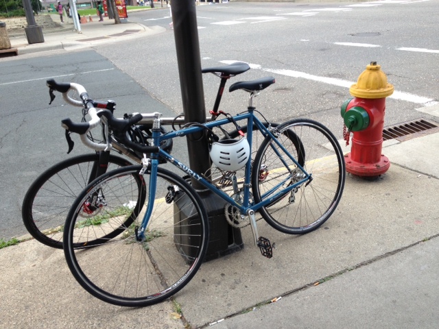 Left side view of a blue Surly Pacer bike on a sidewalk, against a pole, with a fire hydrant behind the back wheel